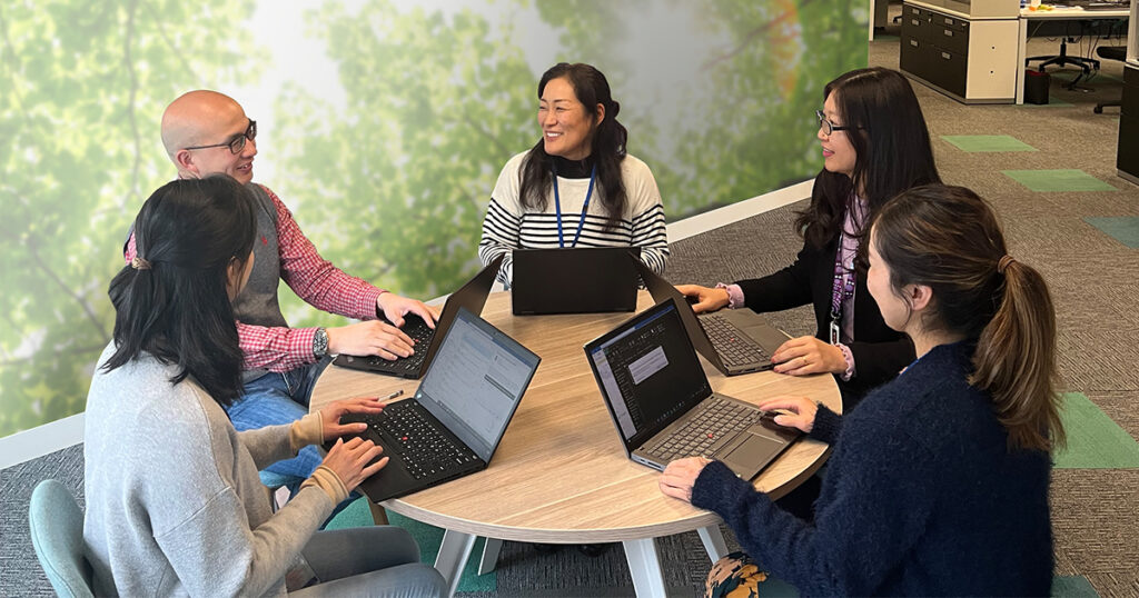 Photo of group of employees with laptops, seated at a round table