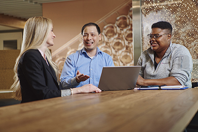 Three employees in conversation around a laptop